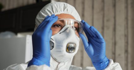 Person in protective gloves and hood putting on glasses