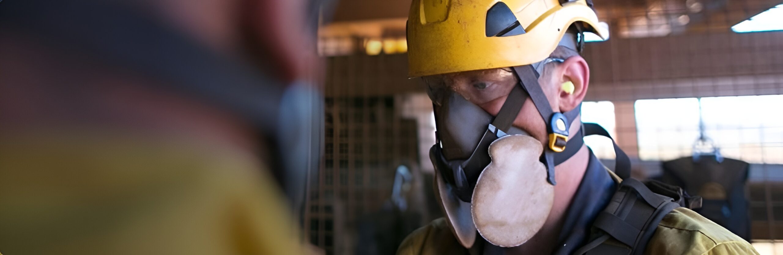 landscape of face of man in warehouse wearing PPE including hard hat and a respirator